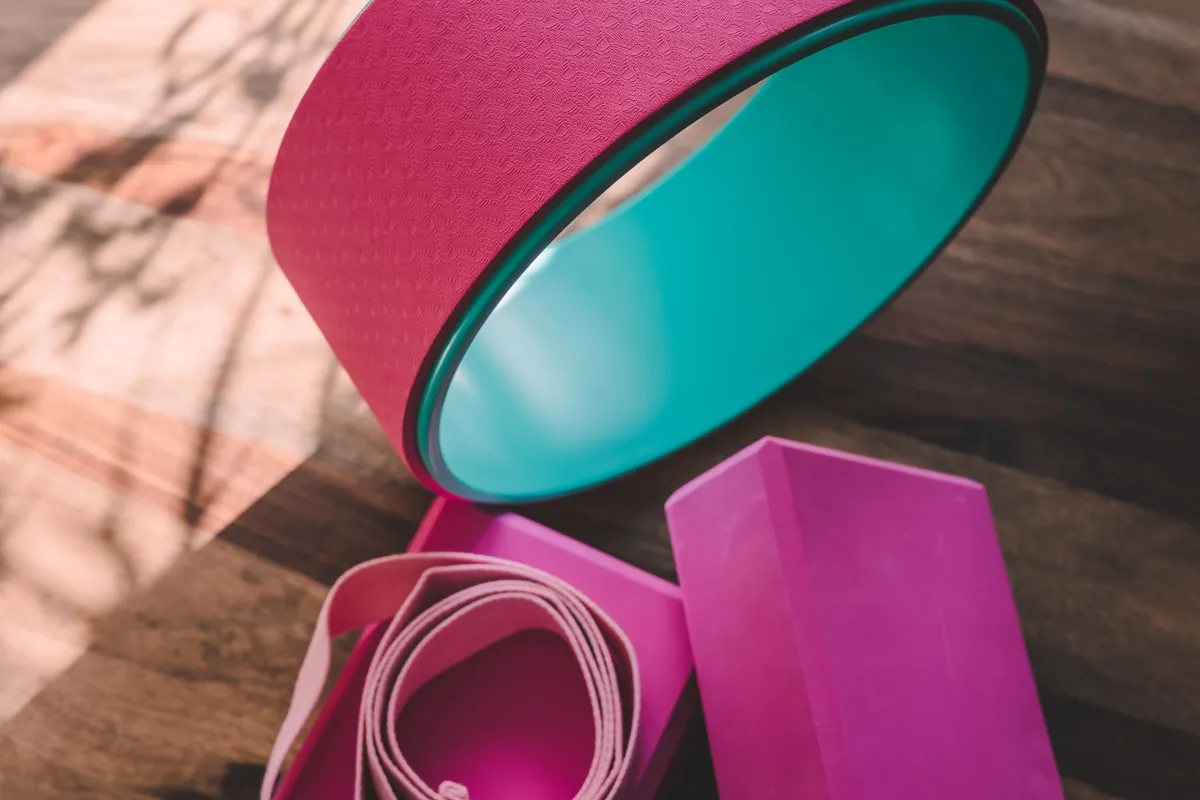 Rózsaszínű jógaeszközök, heveder, jógatéglák és jógakerék a padlón hevernek. 