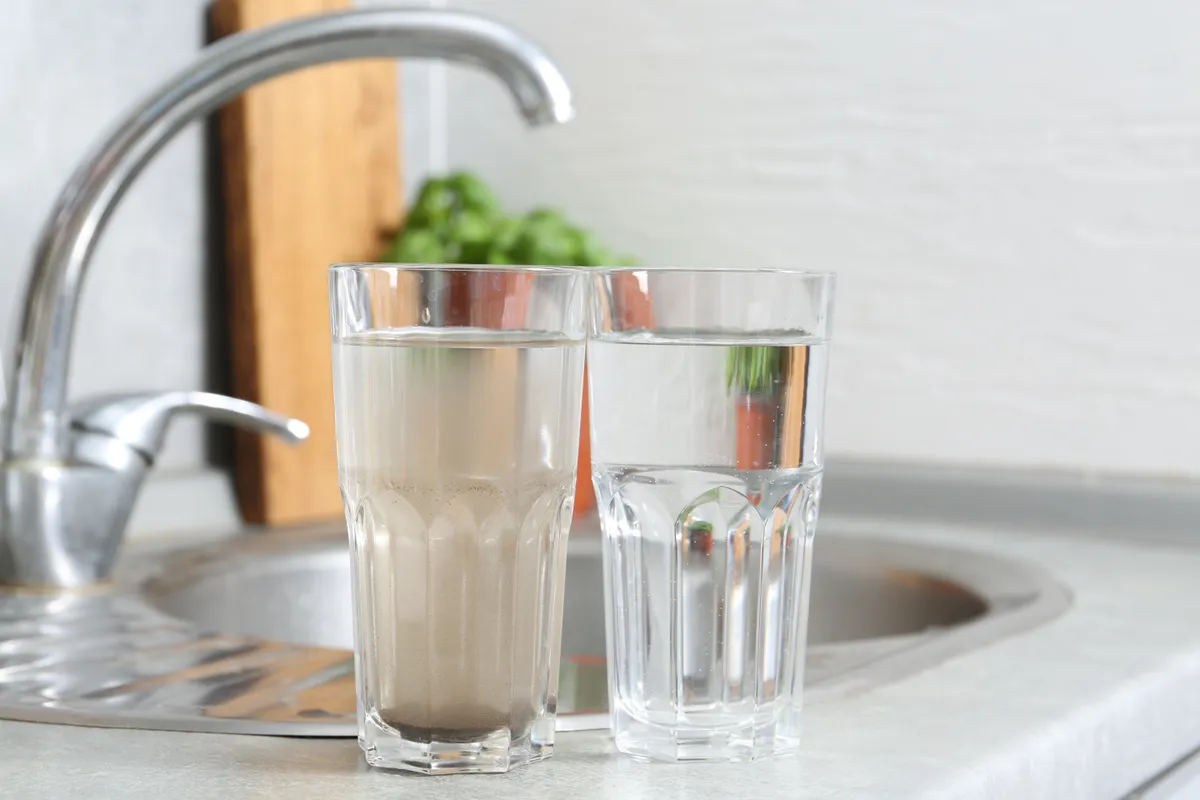 Koszos és tisztított csapvíz két külön pohárban a konyhai csap mellett