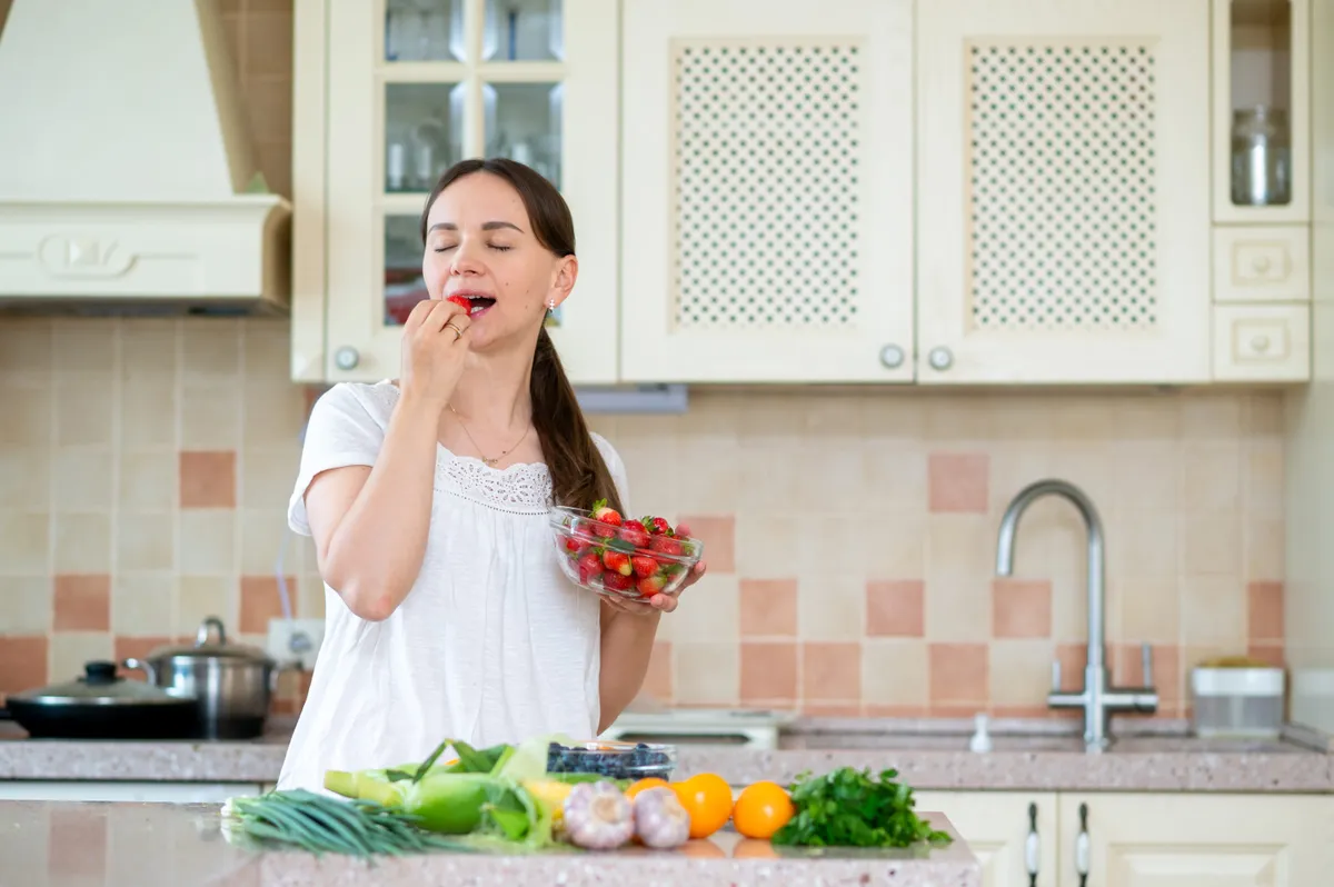 Fiatal nő a konyhában eper csipegetése közben