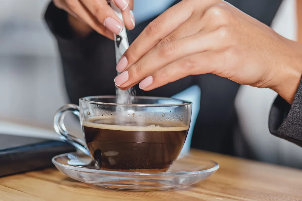 Egy nő cukrot tesz a kávéjába, a kvízben az ételek adalékanyagairól lesz szó. 
