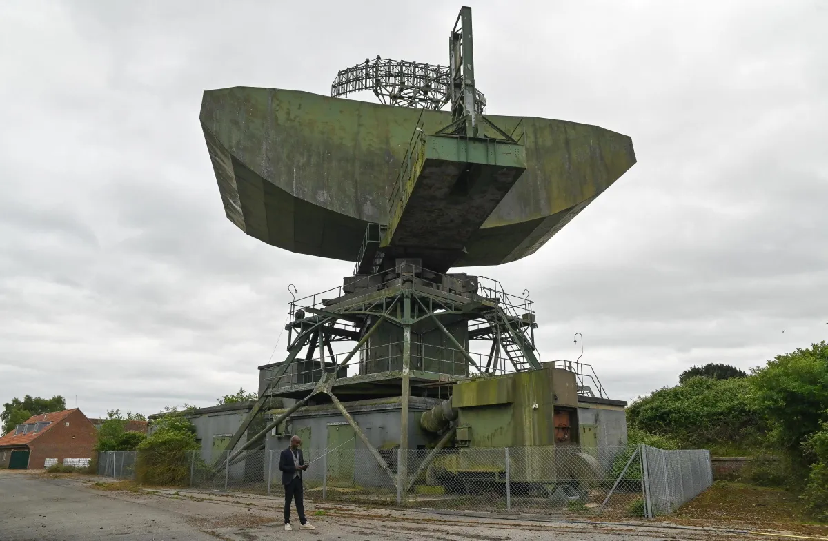 William Sachiti brit tech-milliárdos ufóvadász a hatalmas, zöld, hidegháborús bunker előtt, a tetőn egy hatalmas antennával