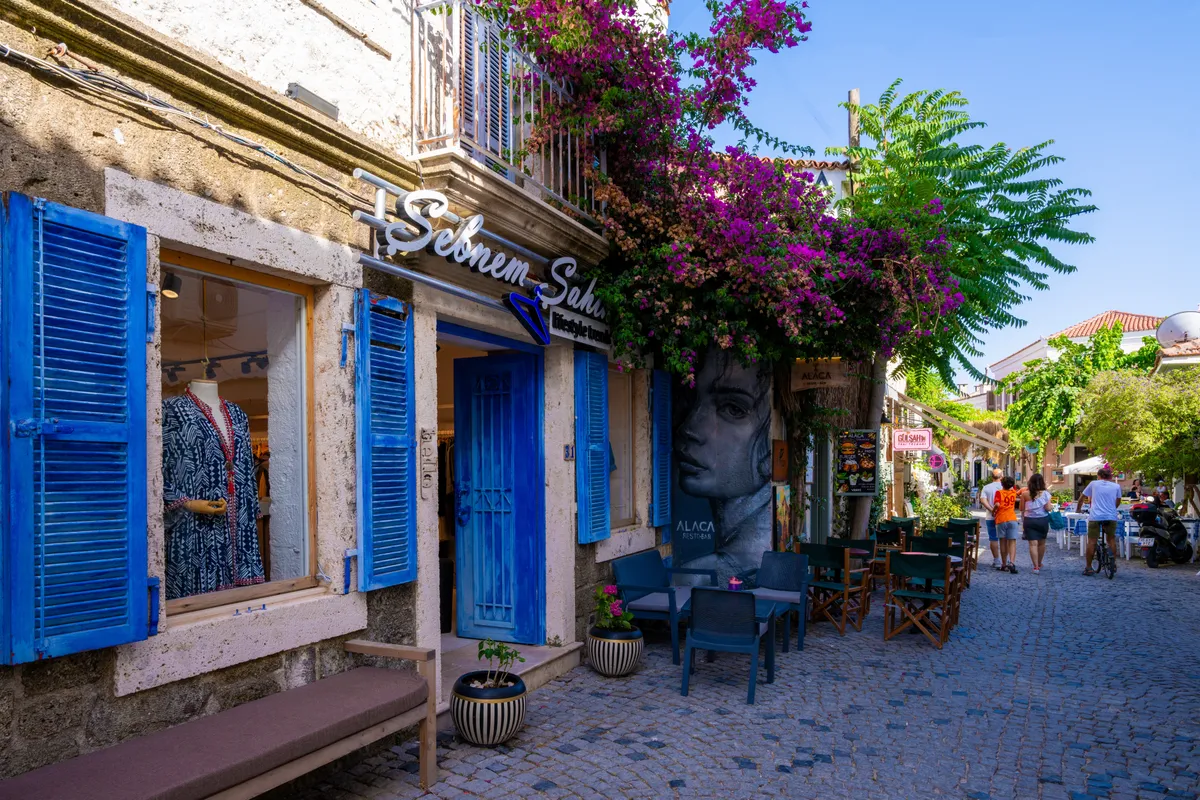 Alaçatı utcarészlet üzlettel és sétáló turistákkal.