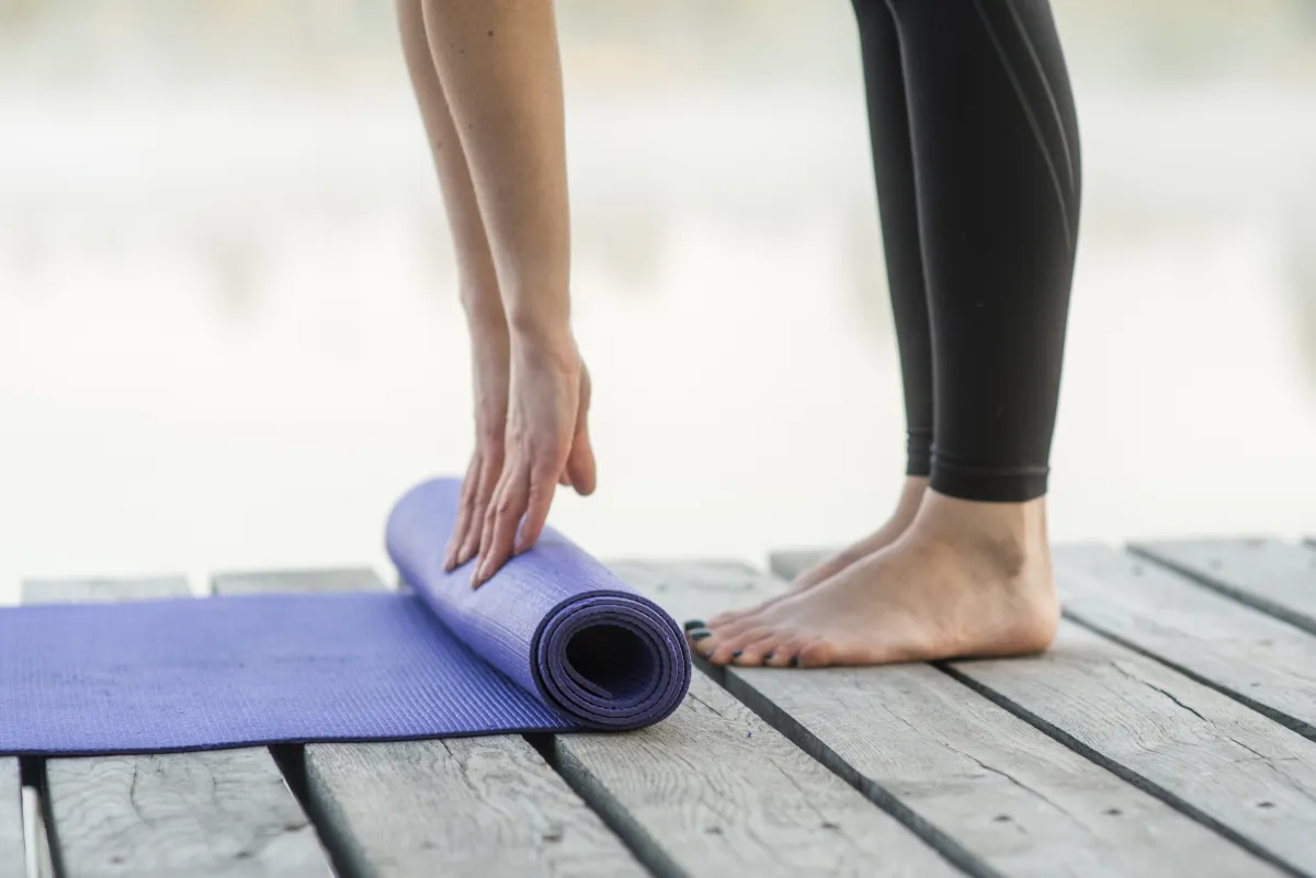 Jógamatracot görget fel egy nő, a kezei és a lábai láthatók.