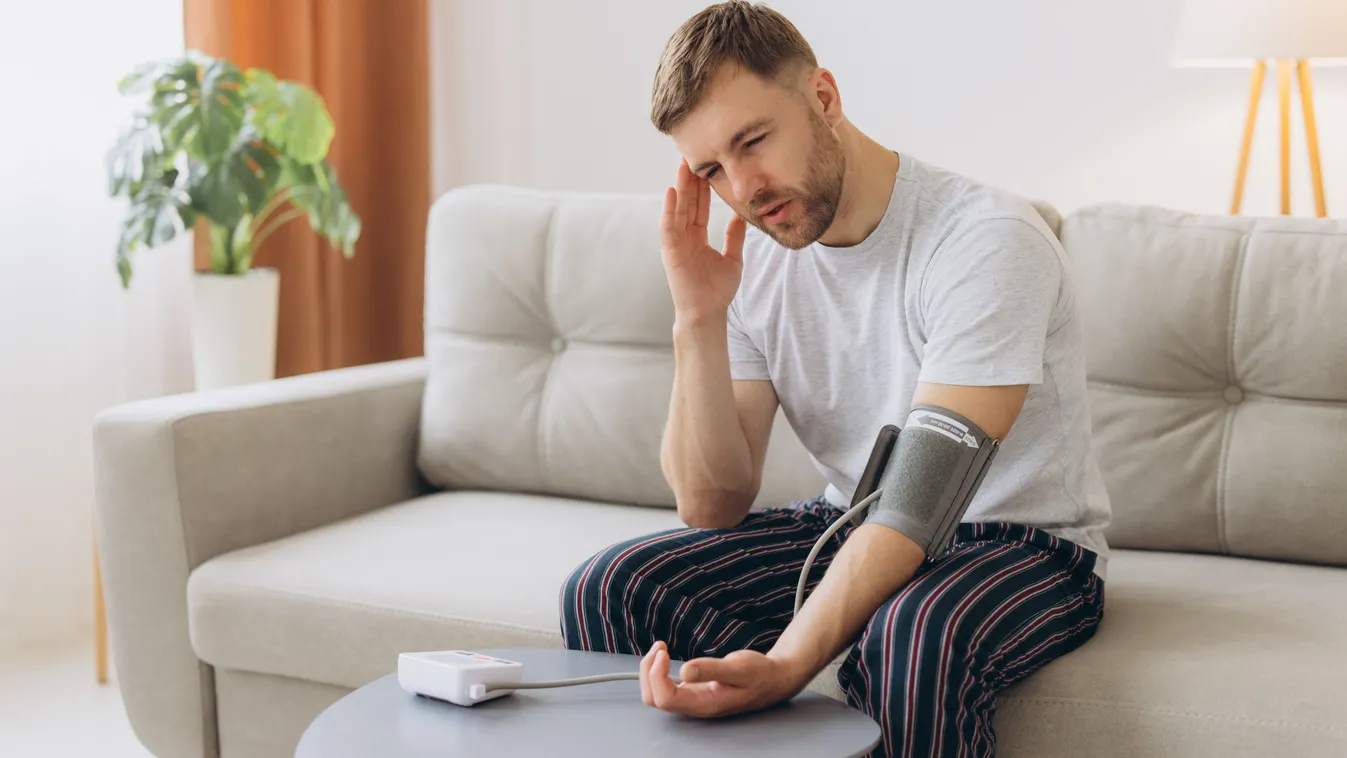 Magas vérnyomás okain gondolkodó fiatal férfi vérnyomásmérés közben