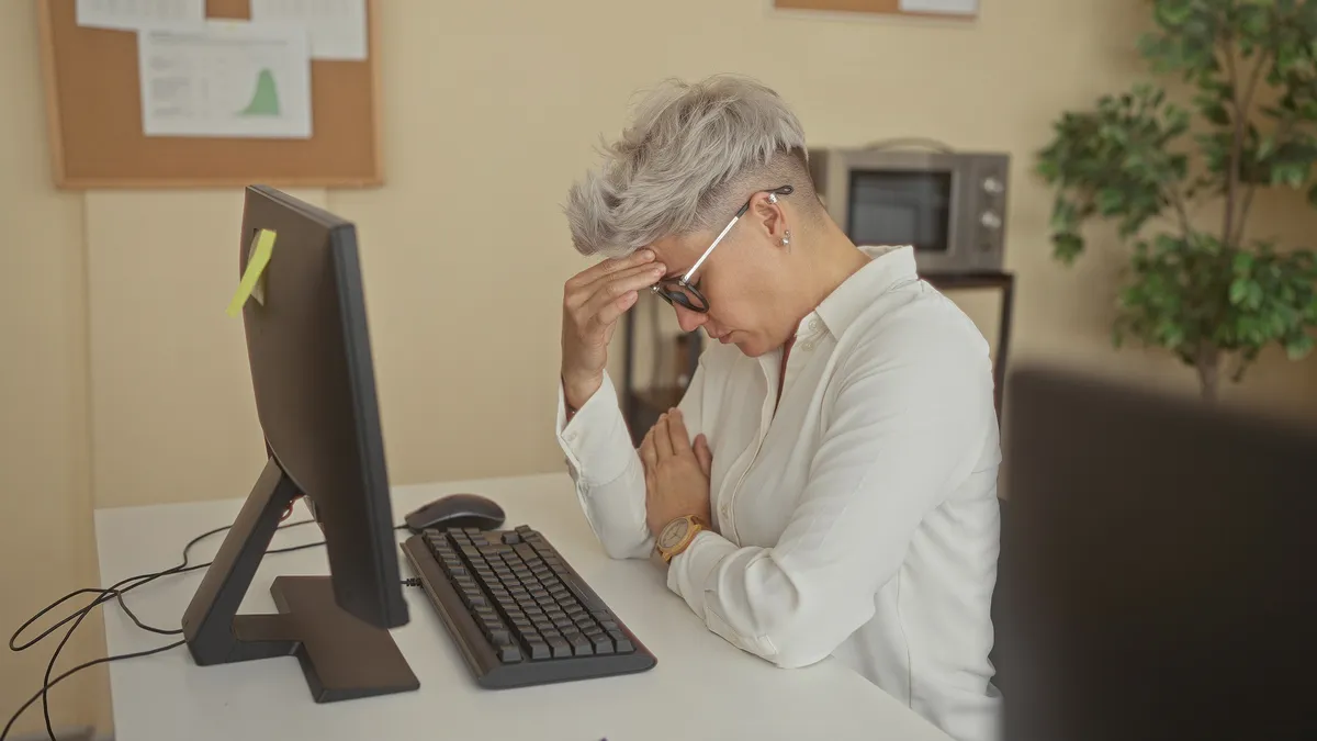 Monitor előtt ülő nő fejfájással