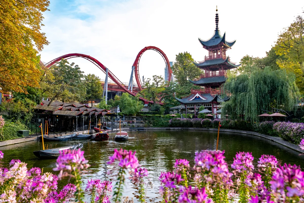 A koppenhágai Tivoli park pagodája és tava virágokkal és hullámvasúttal.