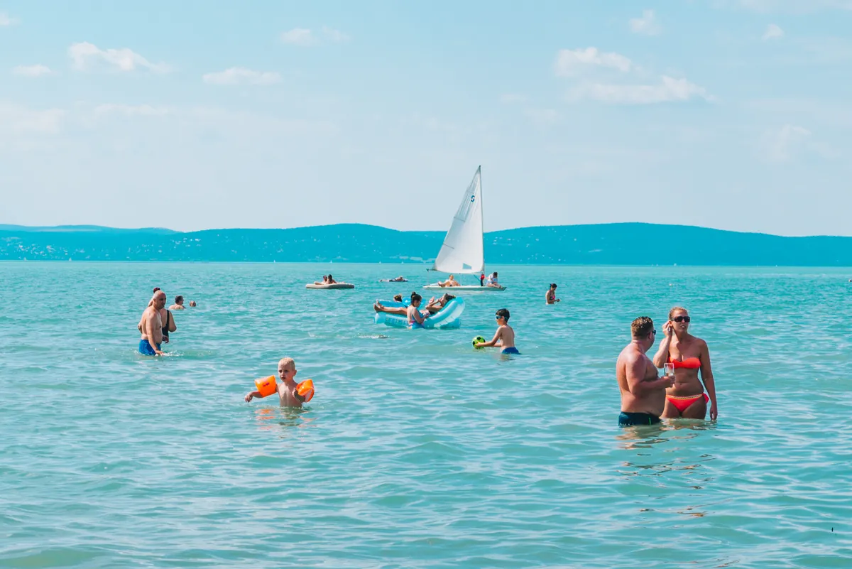 Fürdőző emberek és vitorlás a Balatonban.