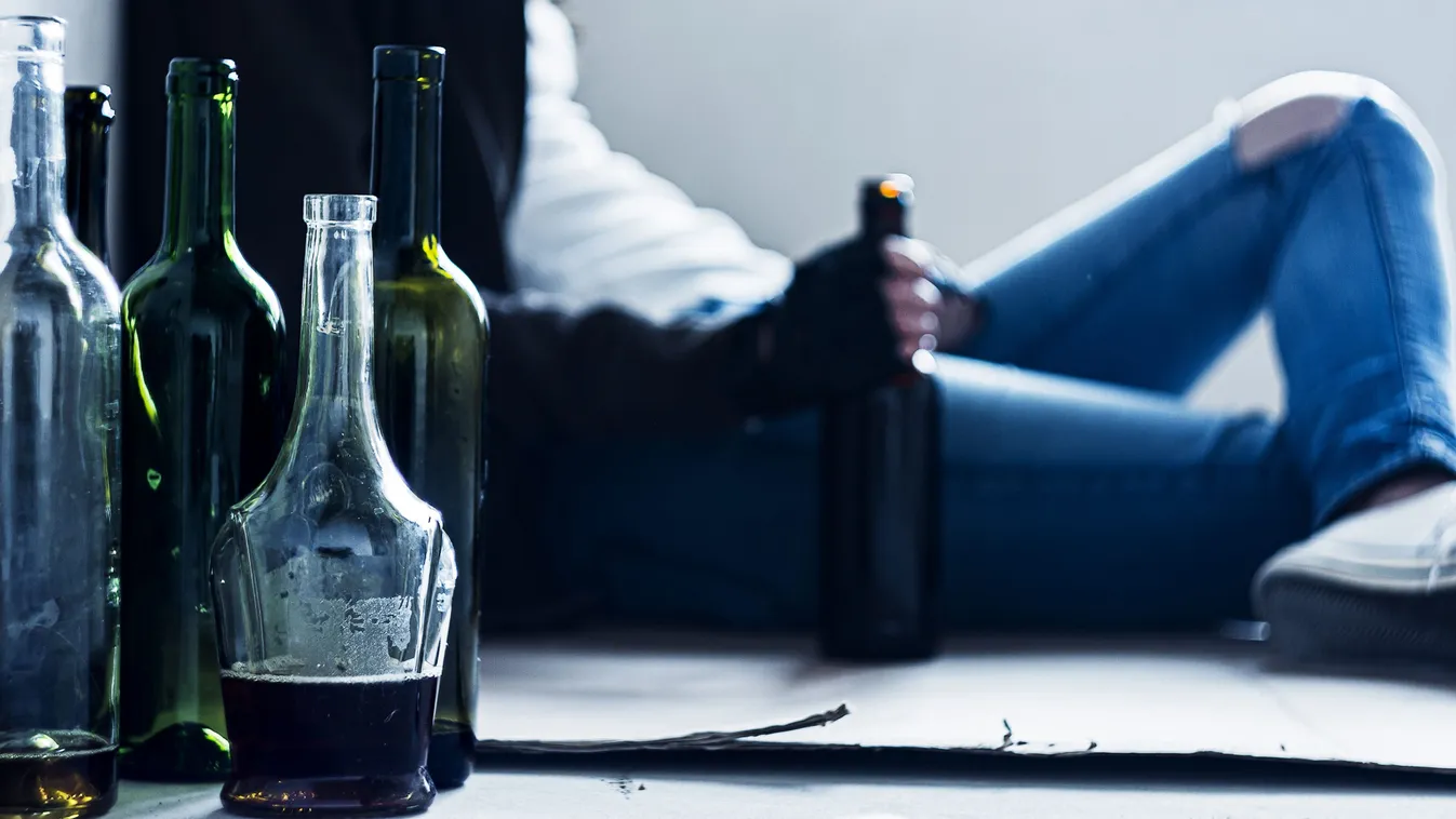 Üres italos üvegek egy alkoholfüggőséggel küzdő férfi otthonában és egy teli üveg a kezében