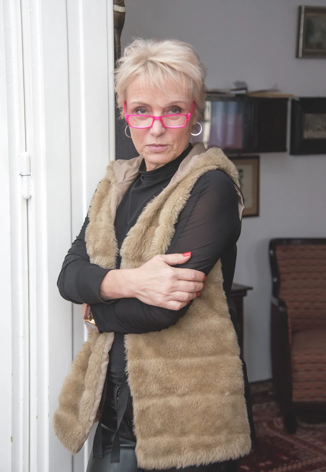Tallós Rita barna mellénybundában piros keretes szemüvegben komoly tekintettel néz a kamerába.