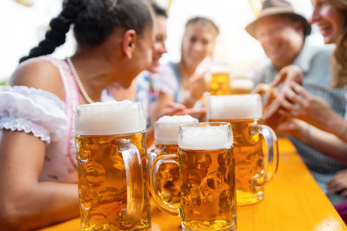 Oktoberfest hangulat sörökkel és dirndlbe öltözött nőkkel egy asztalnál.
