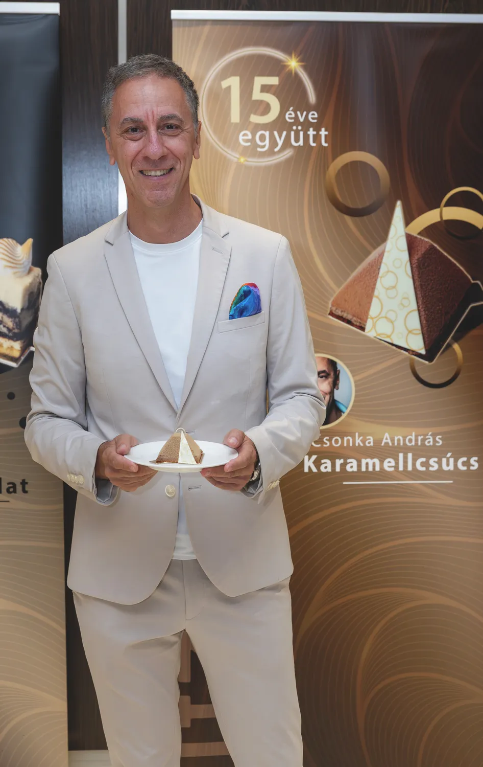 Csonka András krémszínű öltöny szettben tart  akezében egy süteményt.