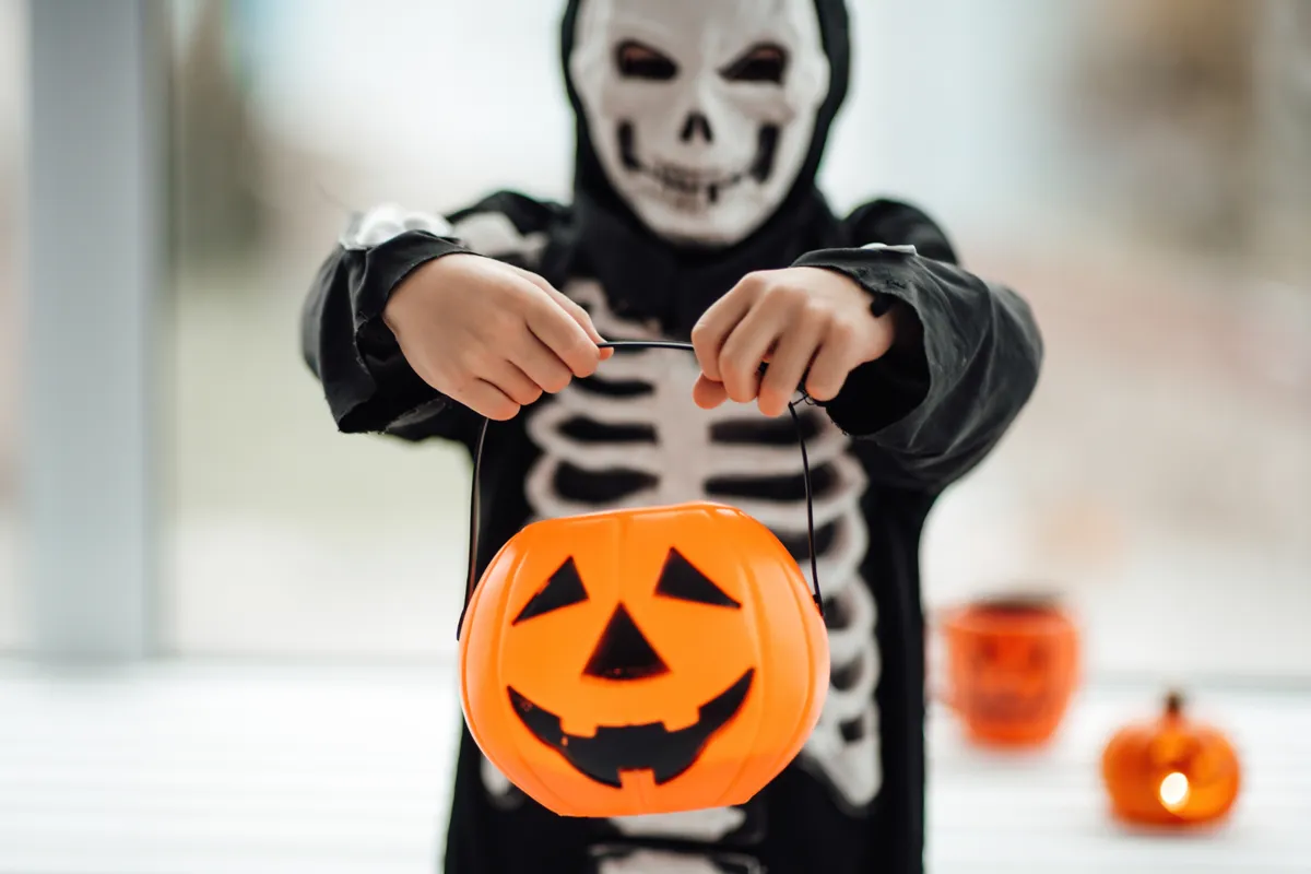 Csontváz öltözetet viselő gyerek Halloween tök-lámpással a kezében.