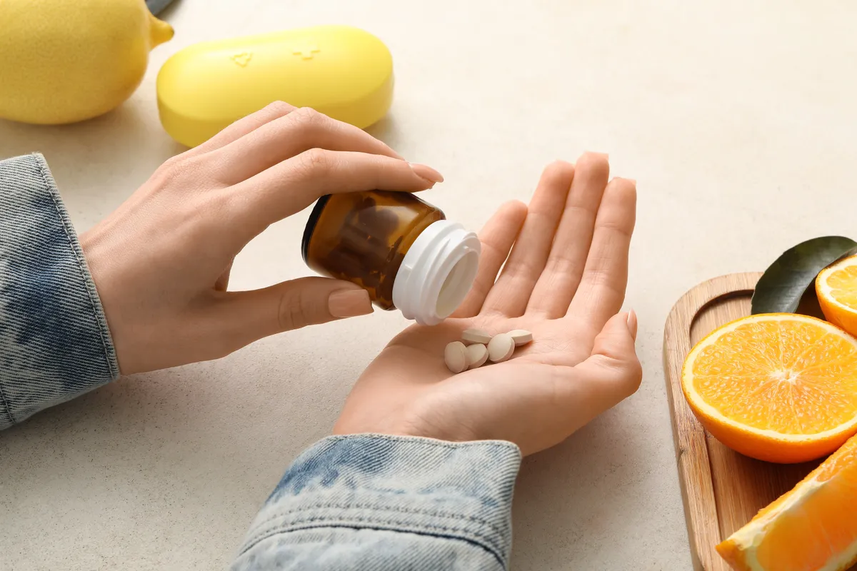 C-vitamin tablettákat önt a tenyerébe egy nő, mellette narancsok vannak felvágva